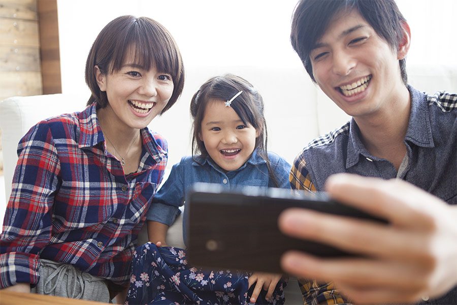 Blog - Happy Family with Young Daughter Sitting on the Sofa at Home Looking at a Phone